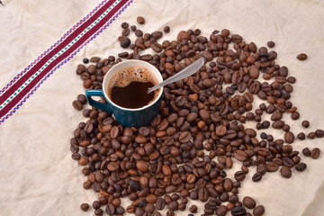 Roasted coffee beans with cup and spoon on jute background. Morn
