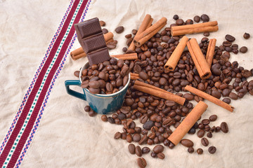 Cup of coffee with cinnamon sticks, bar of chocolate on vintage