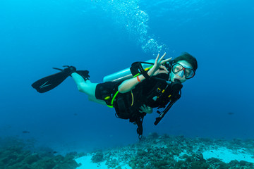 Naklejka na ściany i meble Female scuba diver underwater showing ok signal