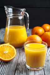Fototapeta na wymiar Glass of freshly squeezed orange juice, ripe oranges and jug on wooden table. Focus on glass.
