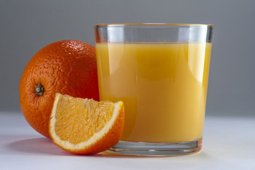 Glass of fresh orange juice and oranges on wooden table.
