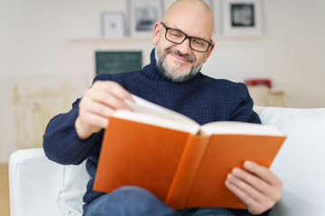 mann mit schwarzer brille liest ein buch zuhause auf dem sofa