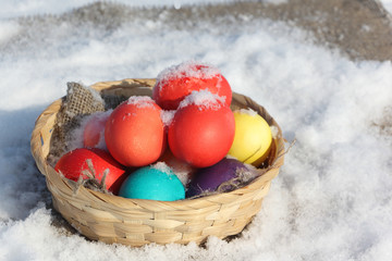 Color Easter eggs in a wooden basket on a napkin in snow
