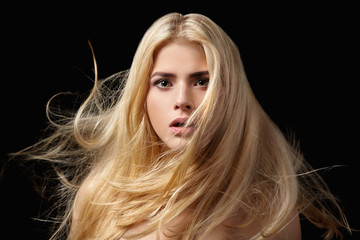Portrait of blonde girl with flying hair on black background