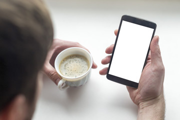Hands of man with coffee on the table with a white screen phone