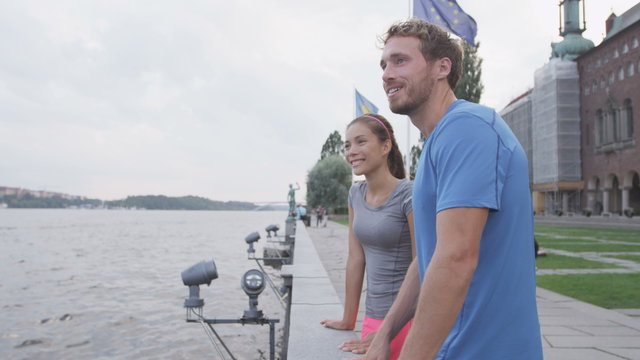 Sporty couple looking at view in Stockholm Sweden. Exercising couple, healthy runners relaxing after running Healthy multiracial asian woman, caucasian man.