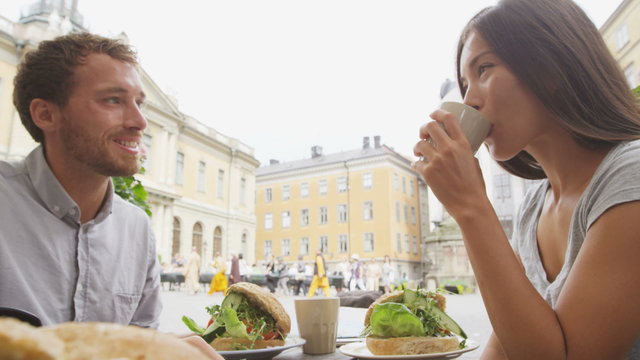 Couple eating food at Cafe in Stockholm, Sweden, Europe. Happy multiracial young couple outside on Stortorget big square in Gamla Stan, the old town of Stockholm. Scandinavian man, Asian woman.