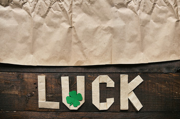 Craft paper origami LUCK lettering on dark barn wood rusctic background. Green clover leaf. St. Patrick's Day greeting postcard template. Space for copy, text, lettering.