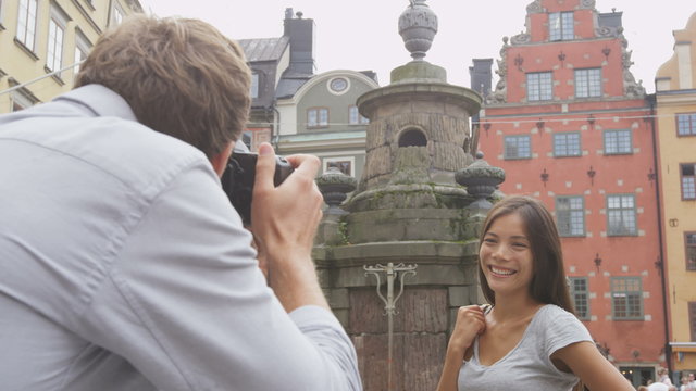 Boyfriend taking picture of girlfriend using SLR camera. Couple in love dating having fun taking photos on travel. Tourists visiting Stockholm, Sweden. Multiracial Asian woman, Caucasian man.