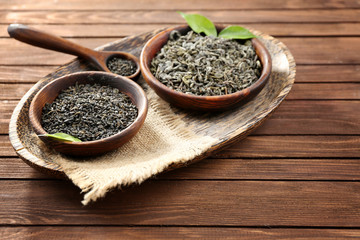 Dry tea in two bowls with green leaves on wooden table background