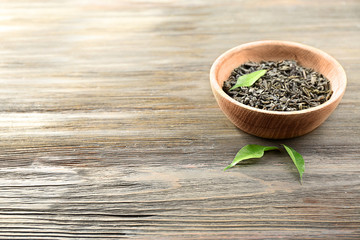 Dry tea with green leaves in bowl on wooden table background, copy space