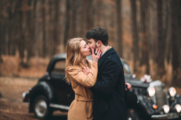 Stylish Loving wedding couple kissing and hugging in a pine forest near retro car
