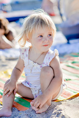 a little girl sits on the beach in the sand and smiles