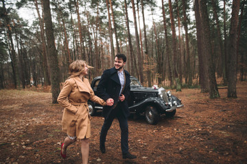 Stylish Loving wedding couple kissing and hugging in a pine forest near retro car