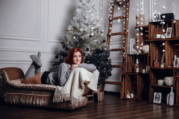 Obraz na płótnie Canvas fashion interior photo of beautiful young woman with red hair and charming smile, wears cozy knitted cardigan, posing beside Christmas tree and presents with chocolate cake with asterisks