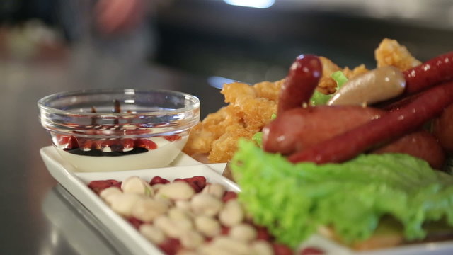 The food on the dish. Beer snacks on a wooden platter. Fried sausages, pistachios, sauce, green leaf lettuce. Squid rings in batter. Restaurant. Pub. Bar.