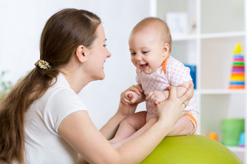 Mother with kid doing exercises with green gymnastic ball at home. Concept of caring for the baby's health.