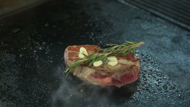 Chef is grilling a steak on the grill. The cook roasts the meat. The rosemary and garlic on the meat. Turns the steak. The preparation of the dish. Restaurant. Food. Marbled meat. Juicy tender meat.