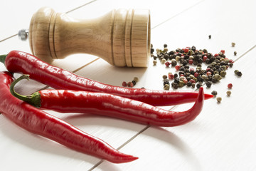 Red pepper and pepper mill peppercorns scattered on a white wooden table