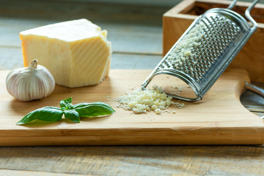 Heap of grated Parmesan on wooden background with leaf of basili