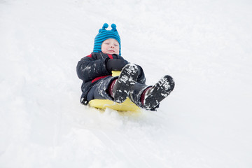 Fototapeta na wymiar Little boy goes to the snowy hills on sleds