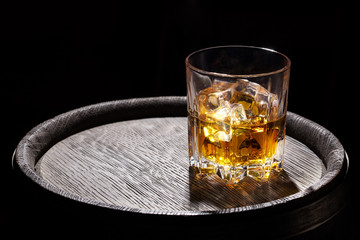 Glass of whiskey with ice on wooden barrel