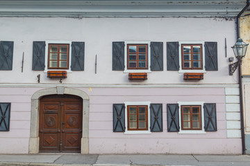 Part of old building facade with windows and opened shutters on them.