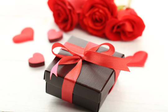 Gift box, rose flowers and decorative hearts on light wooden background