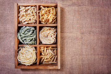 Assorted pasta in wooden box catalog on dark fabric background -