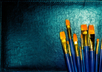 Row of orange paintbrushes of various sizes on blue background abstract