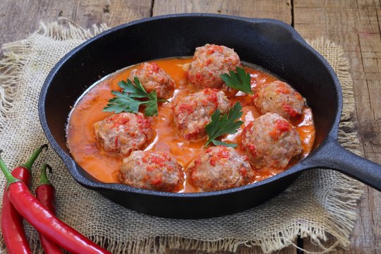 Meatballs in tomato sauce with hot pepper on a wooden table