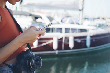 Female's hands with a smart-phone against the background of a moored yacht.