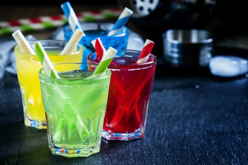 , yellow, red and green alcoholic cocktails with striped straws,