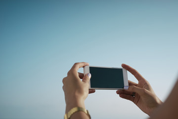 Cropped image of the woman's hands touching a smart-phone display on a sky backgroung