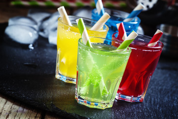 , yellow, red and green alcoholic cocktails with striped straws,