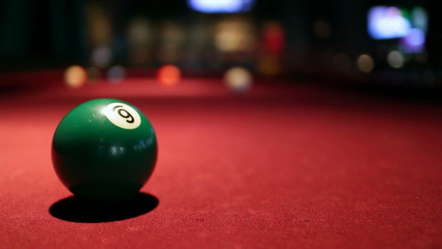 Green six ball in focus on a maroon felt billiard table, in a sports bar