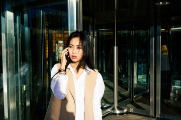 Young attractive asian business woman making a call outside the business center.portrait of a beautiful smiling girl who using smart-phone