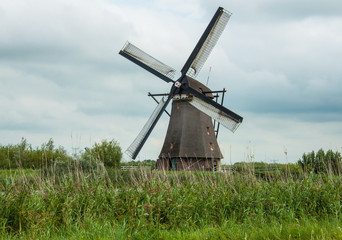 Fototapeta na wymiar Windmill, green land and gray clouds