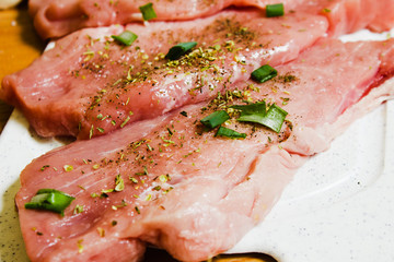 Sliced pork on a white board sprinkled with salt, Italian herbs and onion. Raw pork prepared to cook.