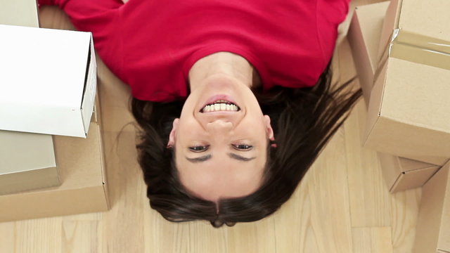High angle view of a young happy woman lying on the floor besides stack of boxes