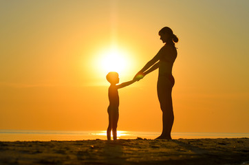 Mother with child sit on the beach at sunset