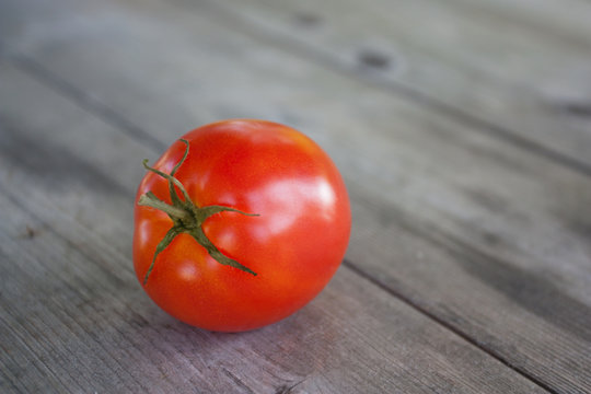 One ripe red tomato on old gray wooden table