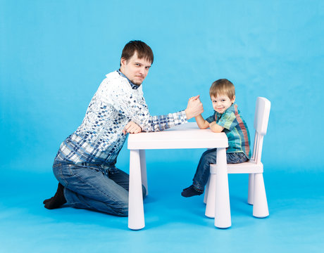 Funny Father And Little Son Competing In Arm Wrestling On Blue