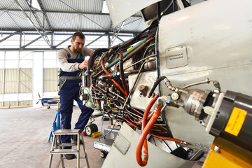 Flugzeugmechaniker repariert die Hydraulik am Triebwerk eines Flugzeuges // Aircraft mechanic repaired the hydraulics on the engine of an airplane - obrazy, fototapety, plakaty
