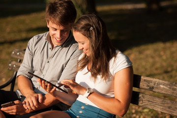 Young couple having fun on a bench in park while socializing ove