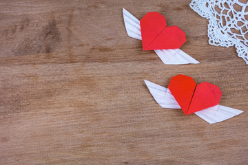 Origami hearts with wings on a wooden background with lace. Two hearts.