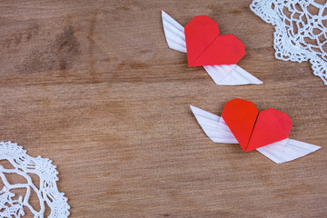 Origami hearts with wings on a wooden background with lace. Two hearts.