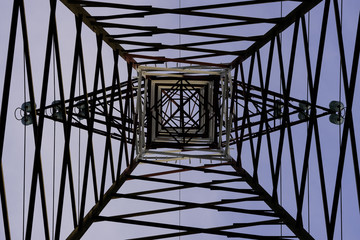 geometria astratta di asta metallica di traliccio alta tensione con sfondo cielo blu visto dall’interno del traliccio guardando verso l’alto 