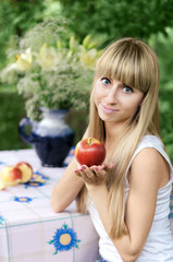 Girl holding Apple, sitting at a table in the garden