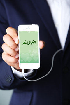Music smartphone with romantic screensaver  in businessman hand, close-up